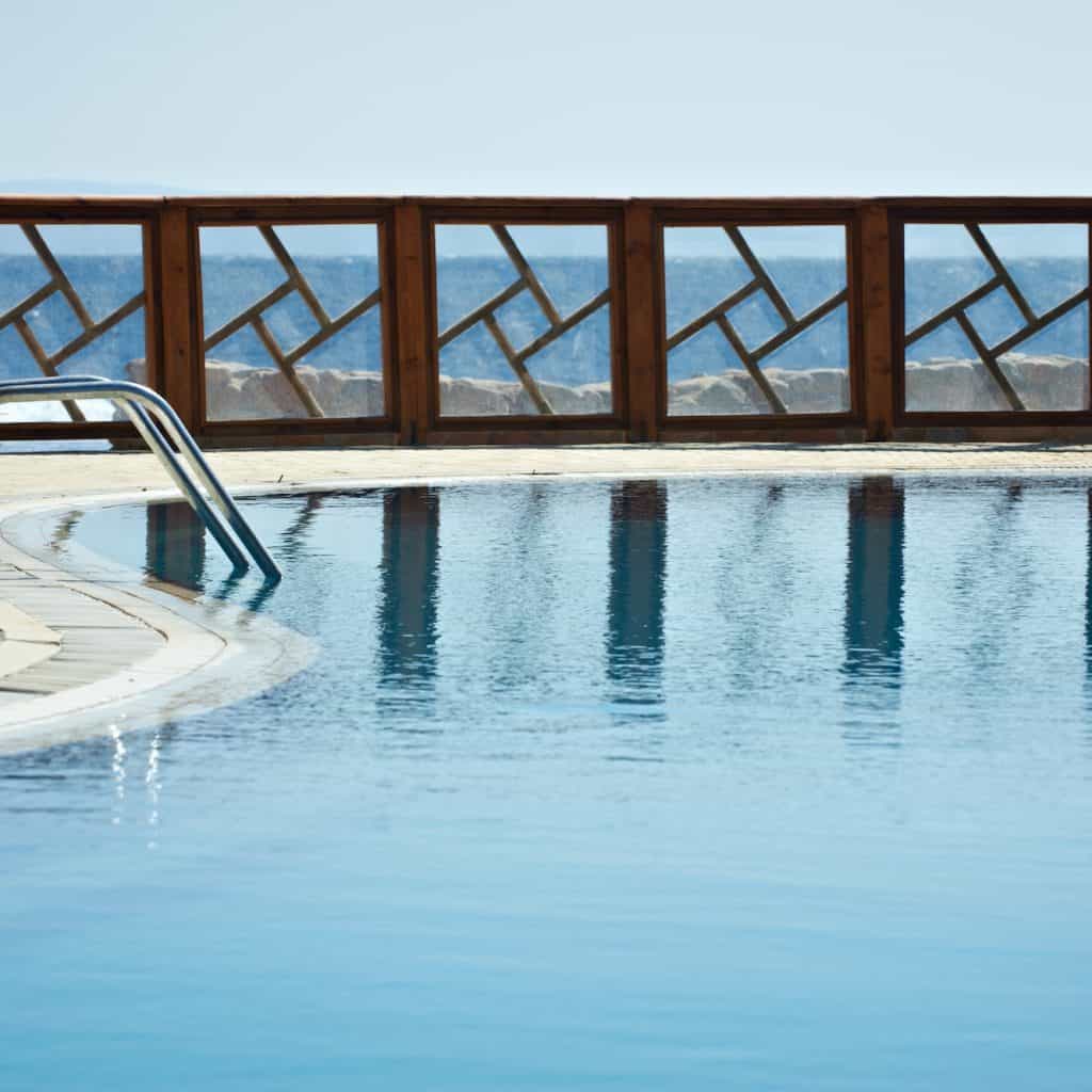 Fence of the resort pool reflected on the water. Pure blue sky on the background. glass rail pool