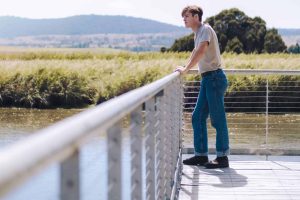 person with cable railing near water and sky